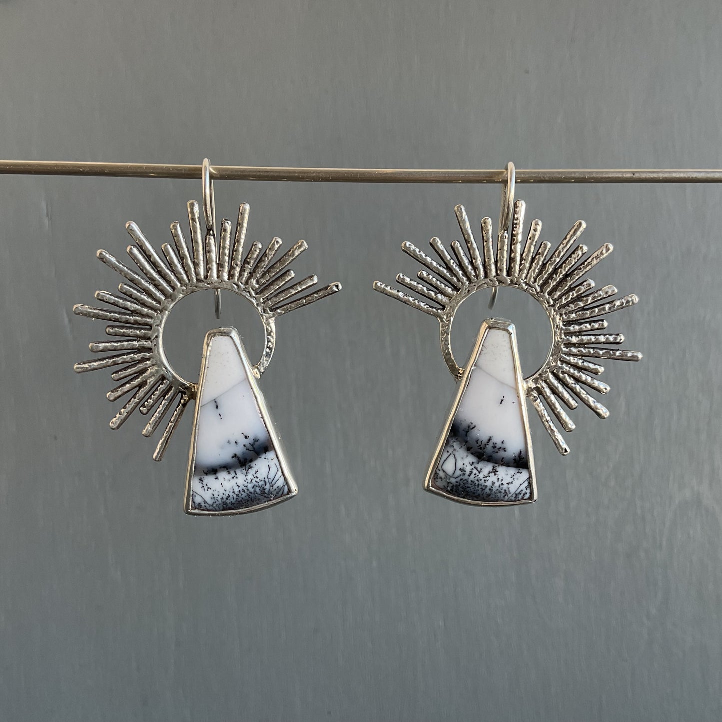 Pair of earrings with sunburst design and marble-like stone on a gray background
