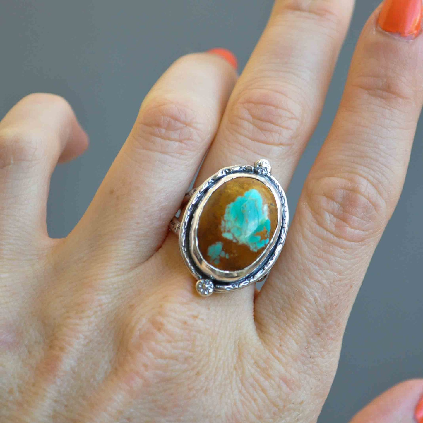 Silver ring with a turquoise stone on a hand against a gray background
