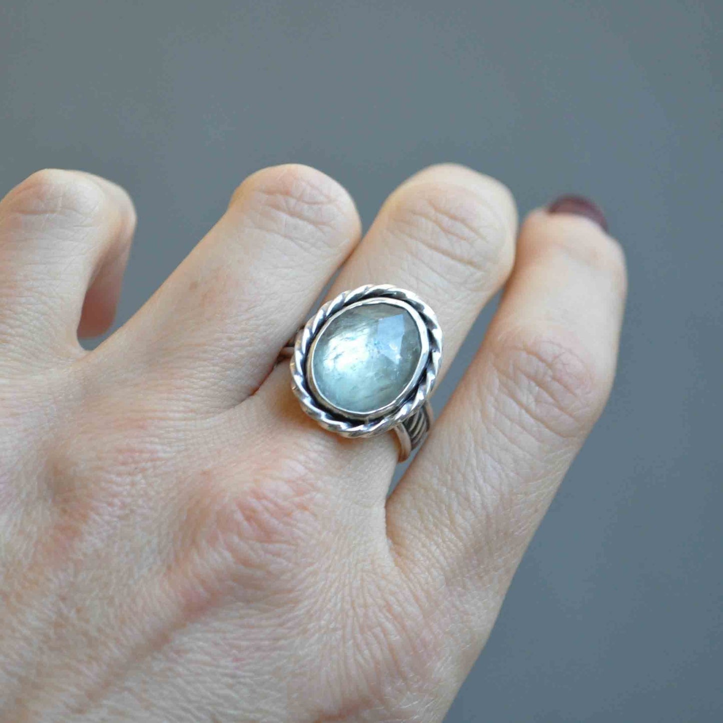 Silver ring with a gemstone on a finger against a gray background