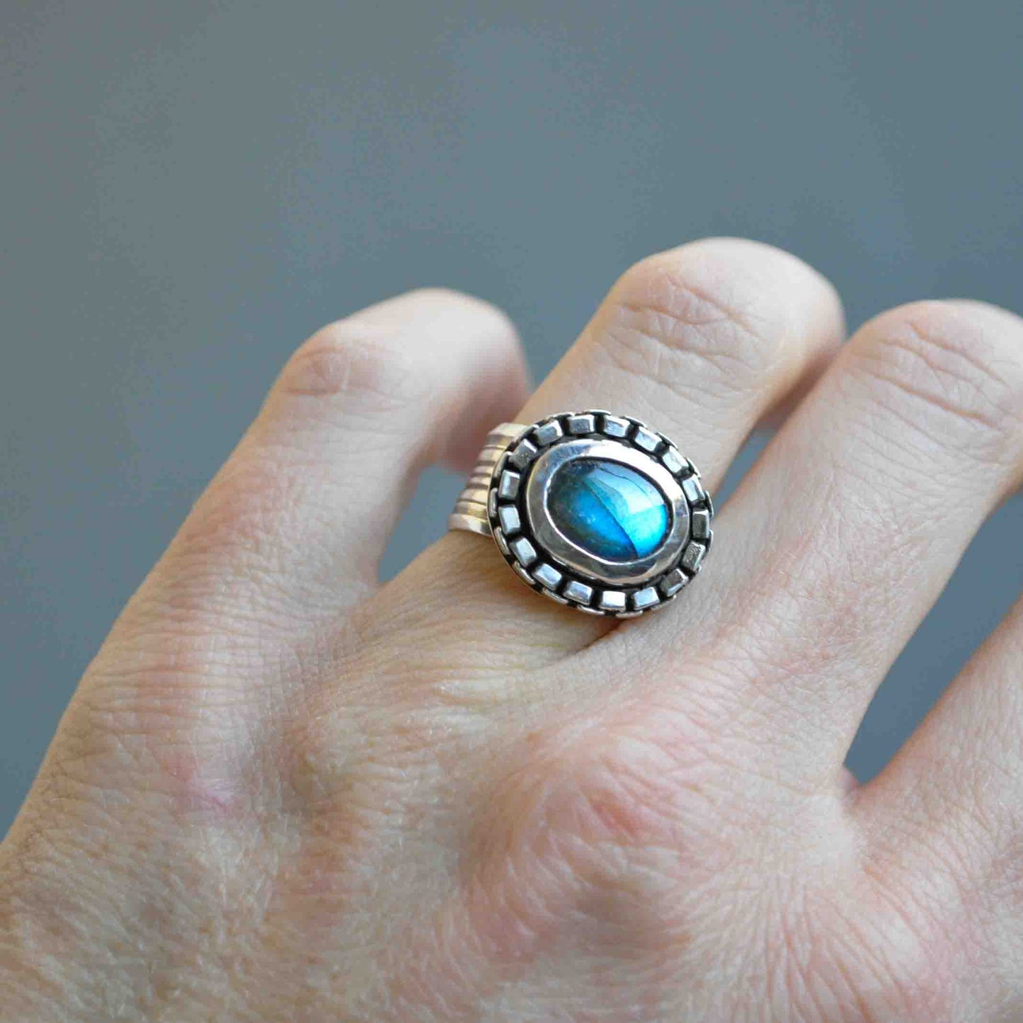 Silver ring with a blue gemstone on a finger against a gray background