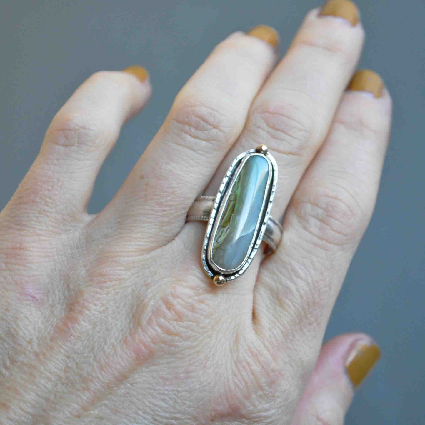 Hand wearing a ring with a large stone on a gray background