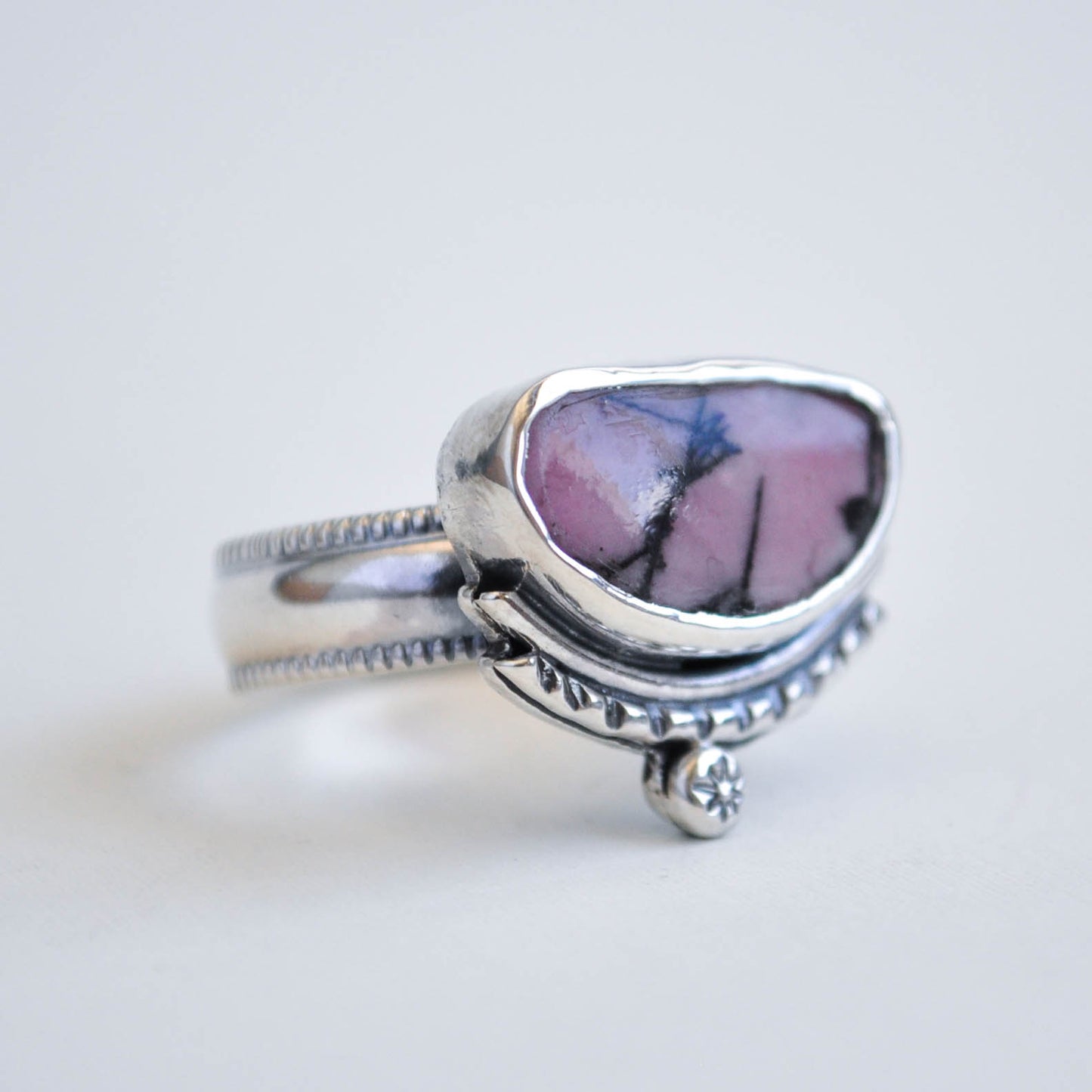 Silver ring with a pink and purple stone on a light gray background