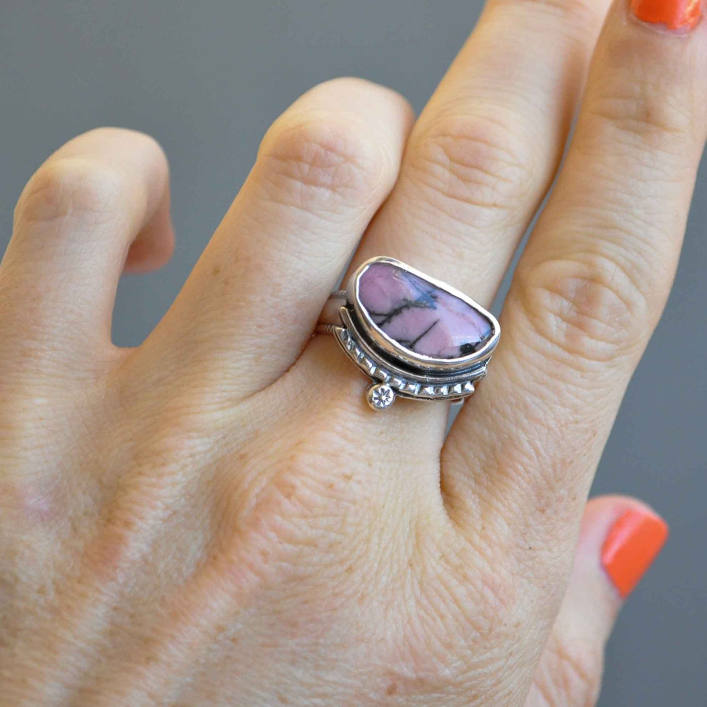 Hand wearing a silver ring with a purple stone on a gray background