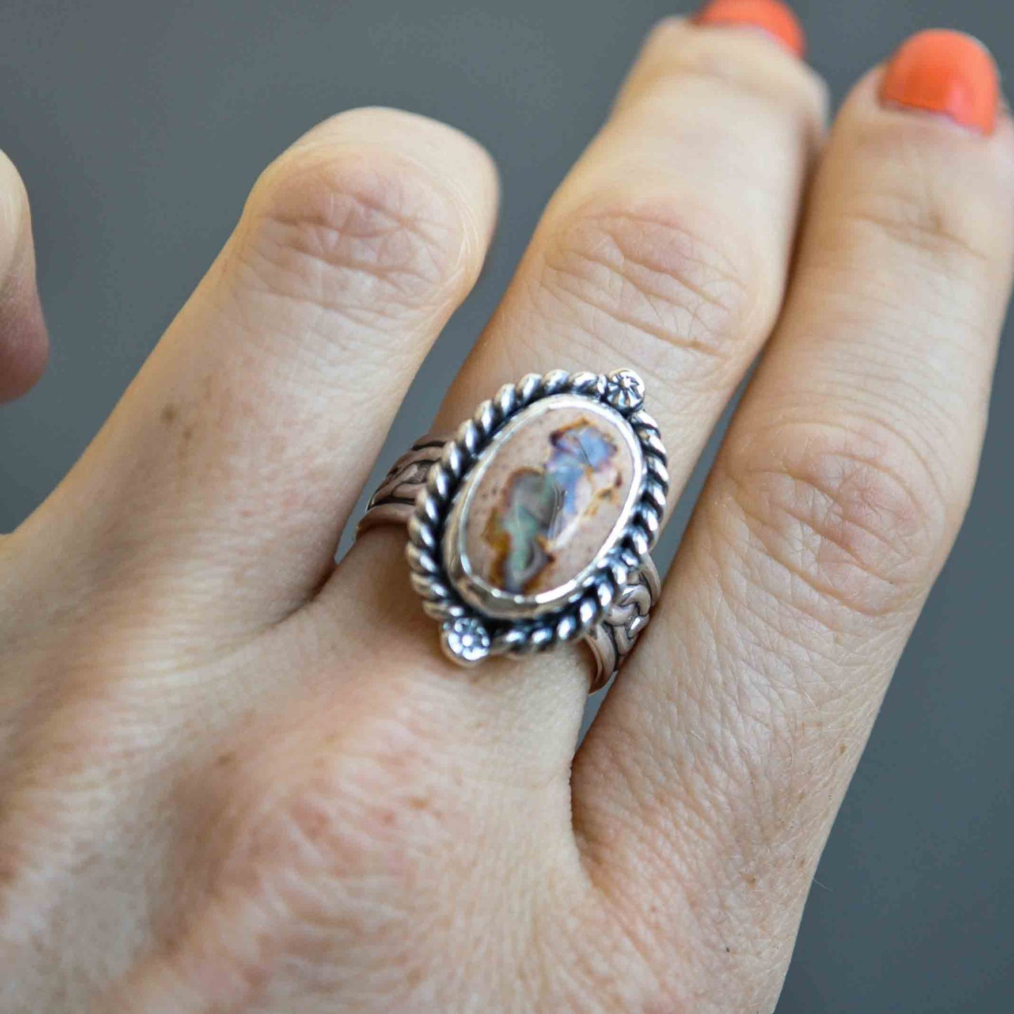 Silver ring with a decorative design on a person's finger against a gray background