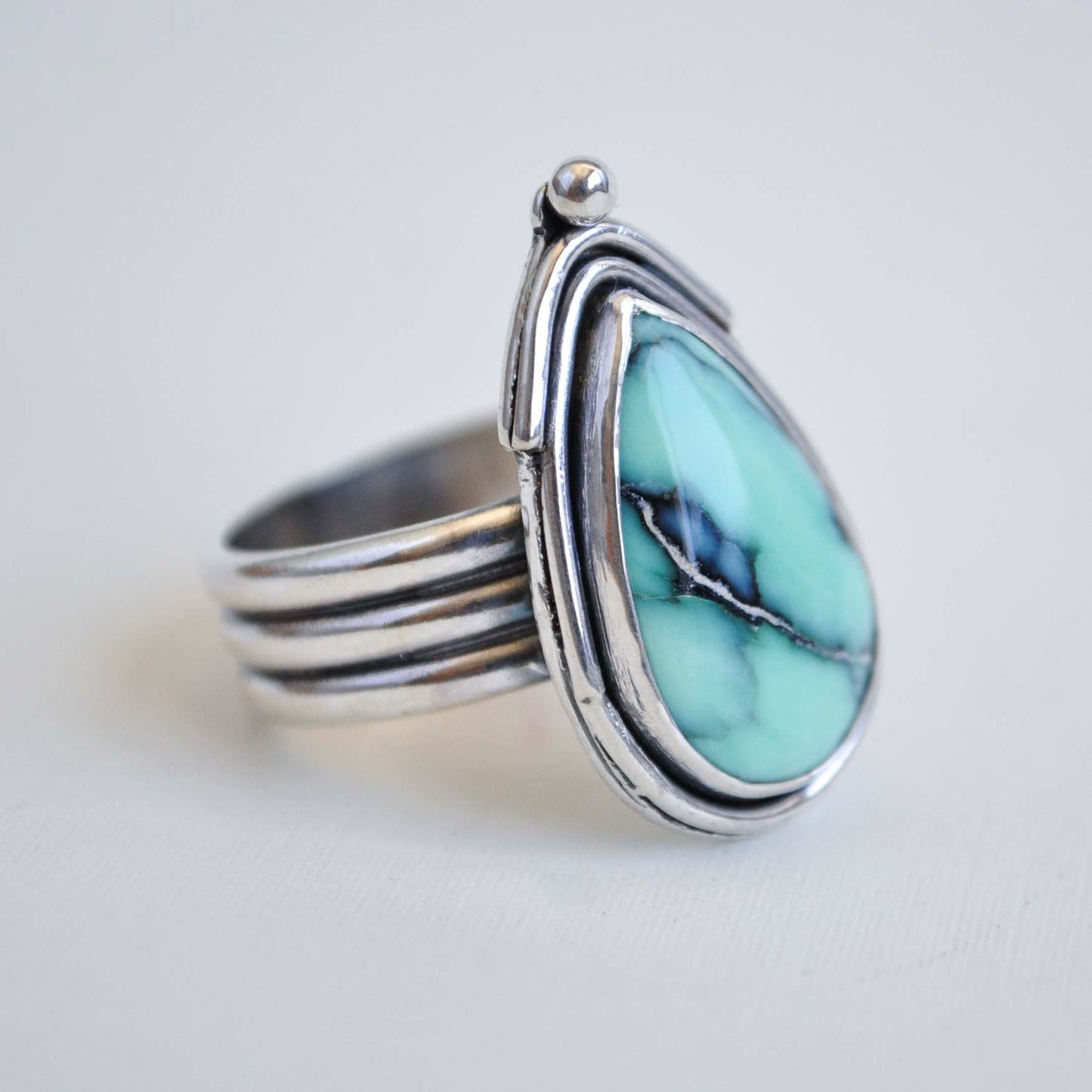 Silver ring with a turquoise stone on a light gray background