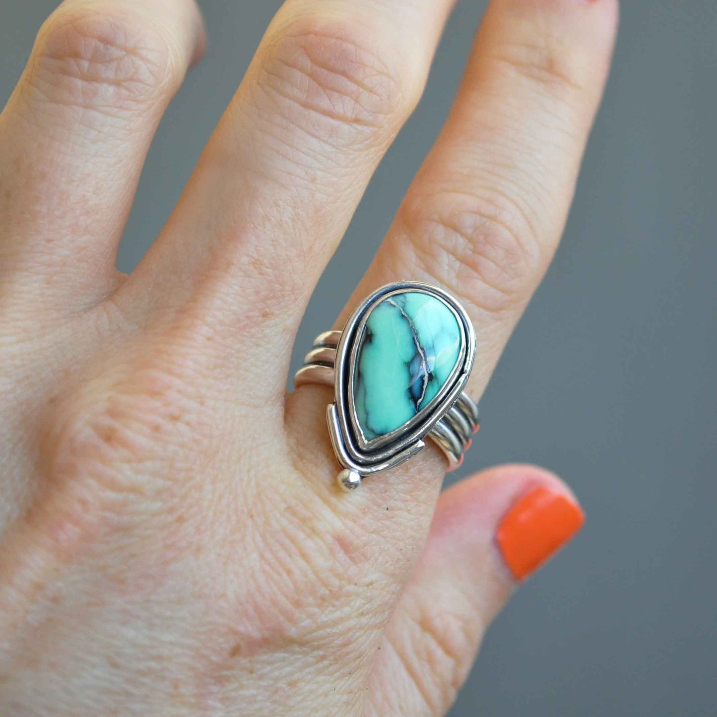 Turquoise stone ring on a finger with a gray background