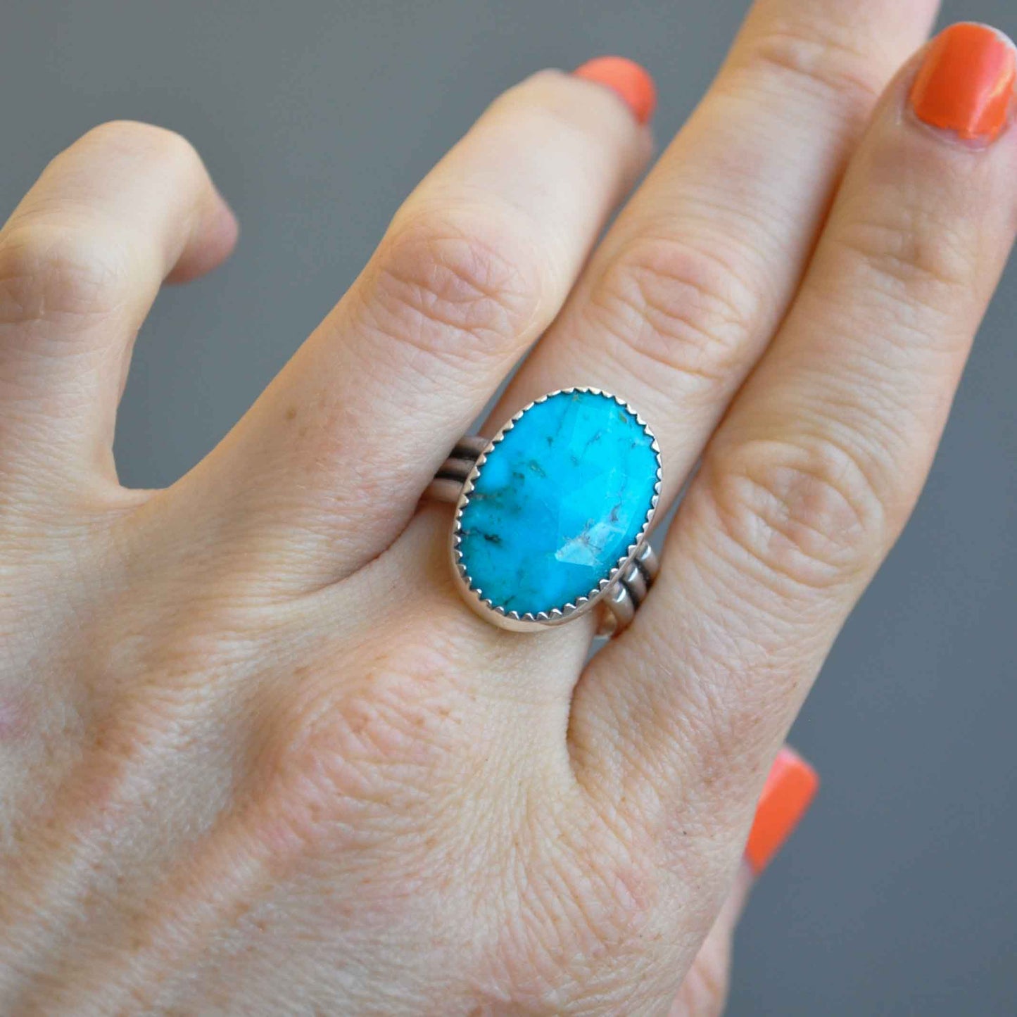 Hand wearing a turquoise ring with a gray background