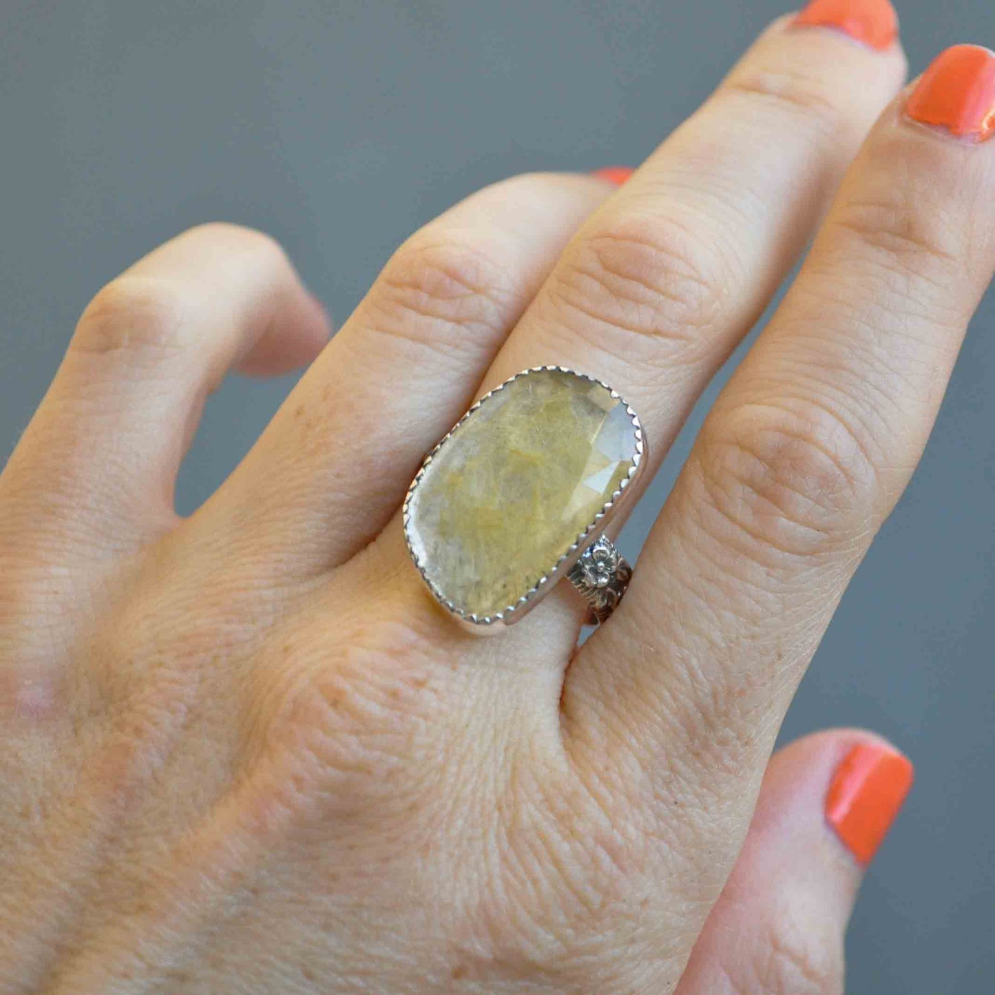 Hand wearing a large ring with a stone on a gray background