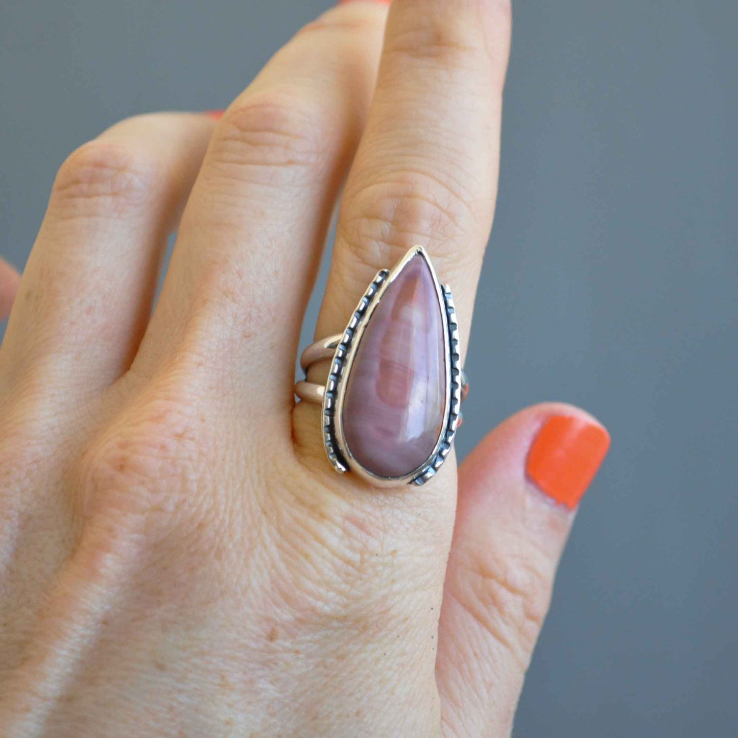 Hand wearing a ring with a purple stone on a gray background