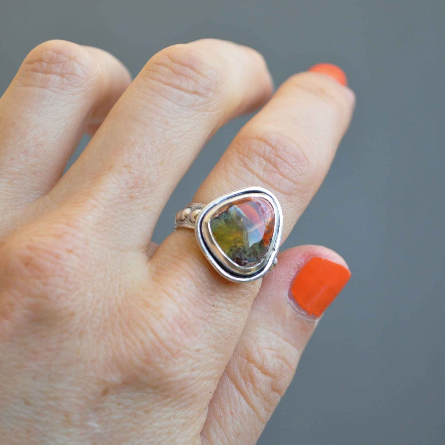 Hand wearing a ring with a colorful stone on a gray background