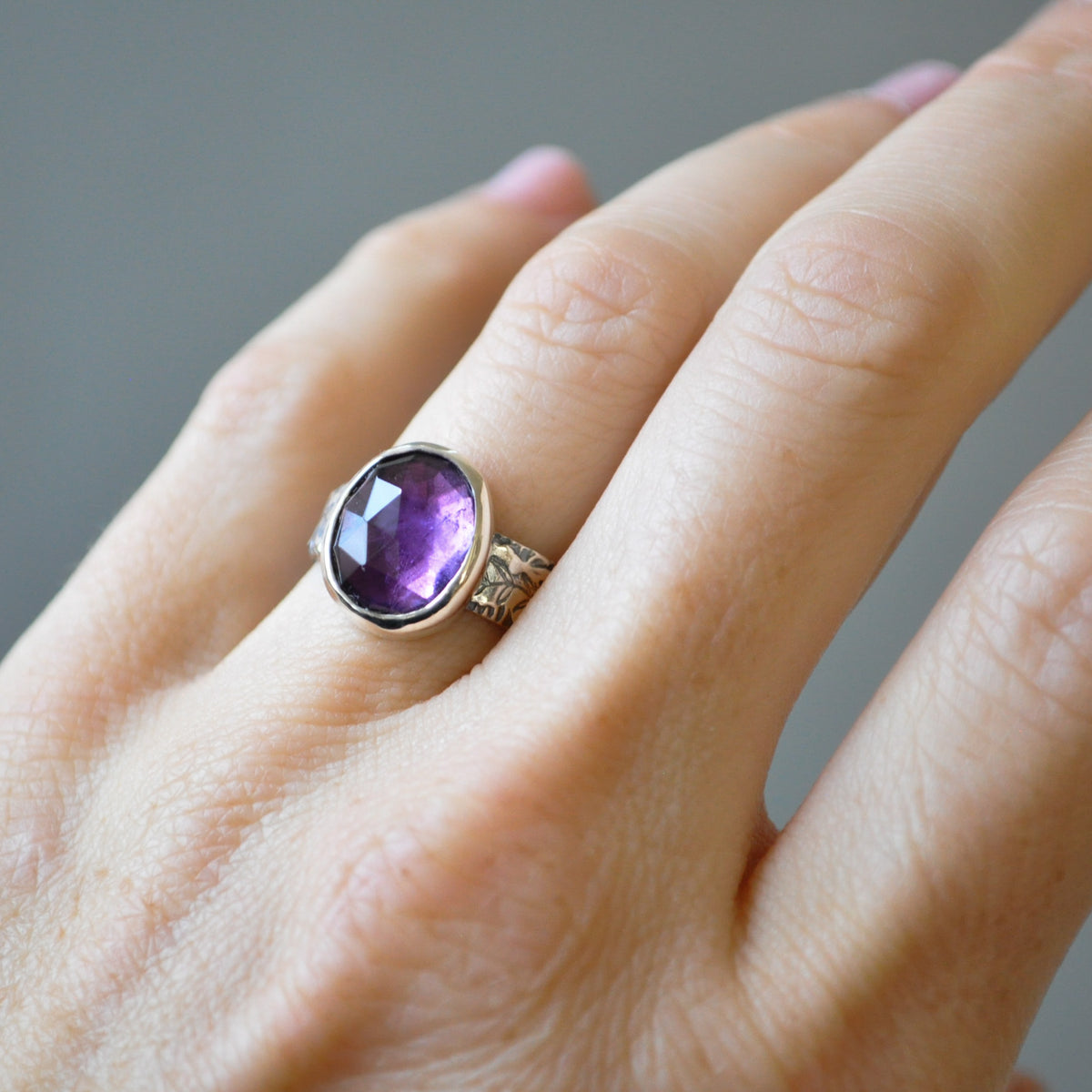 A close-up of a hand wearing a silver ring with a large oval-cut amethyst gemstone.