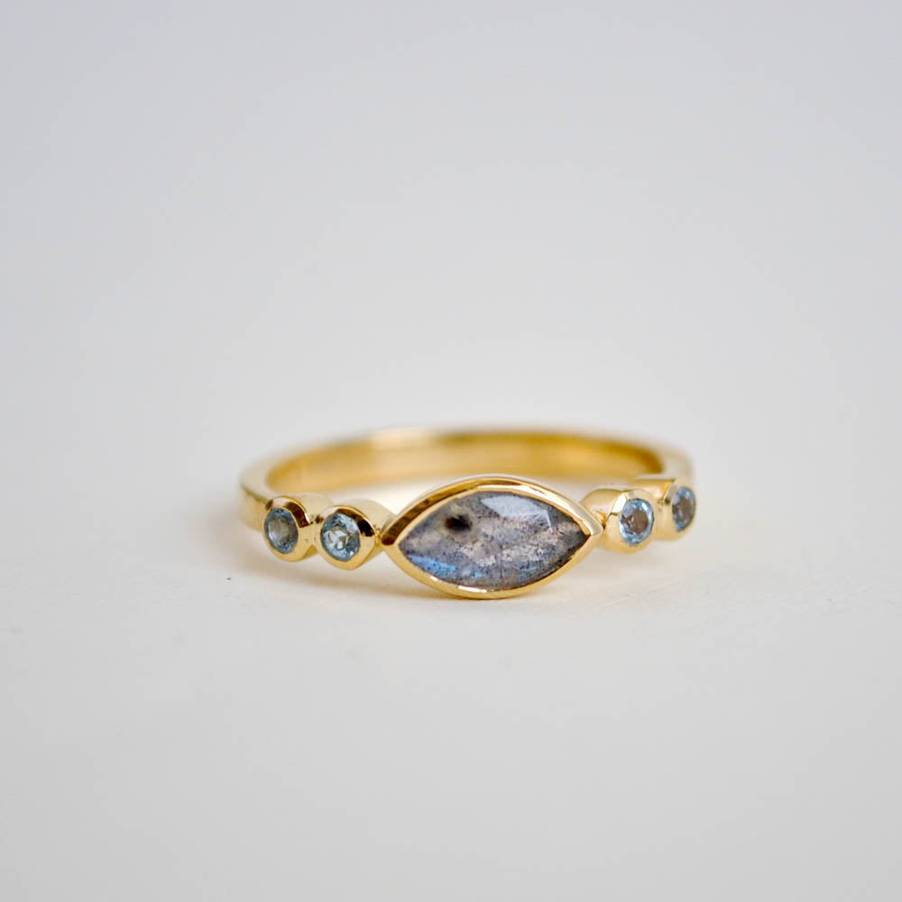 Flashy larbradorite marquise gemstone centered between two sets of round swiss blue topaz gemstones on a plain half round band in 14k gold vermeil and sterling silver