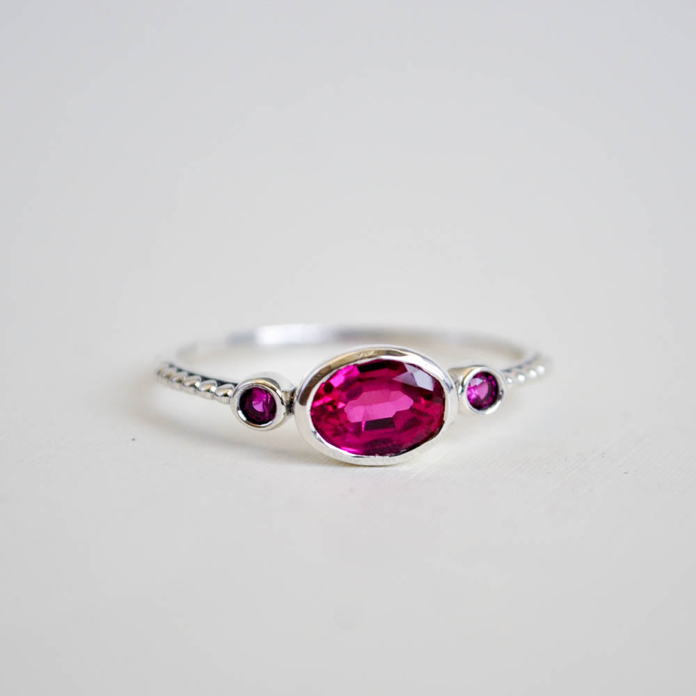 Faceted ruby gemstone bezel set with two round rubies on either side, on a dotted sterling silver band.