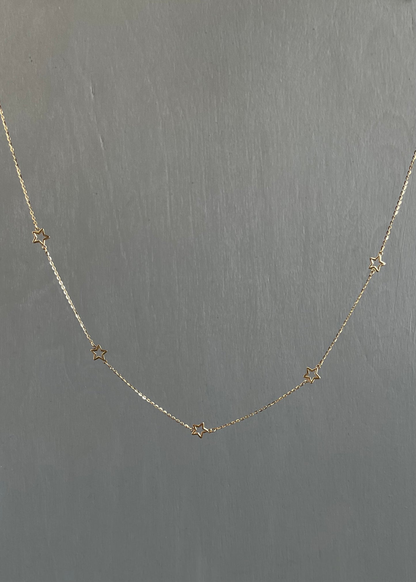 Delicate gold necklace with star-shaped pendants on a gray background