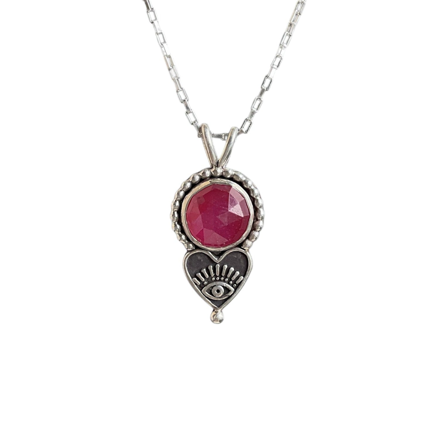 Round ruby gemstone pendant with a beaded border and heart eye embellishment on a sterling silver chain