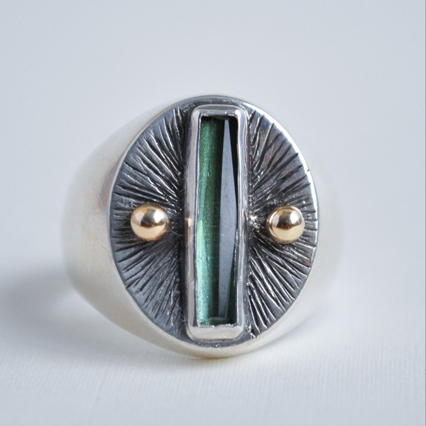 Silver ring with green central stone and gold accents on a light gray background
