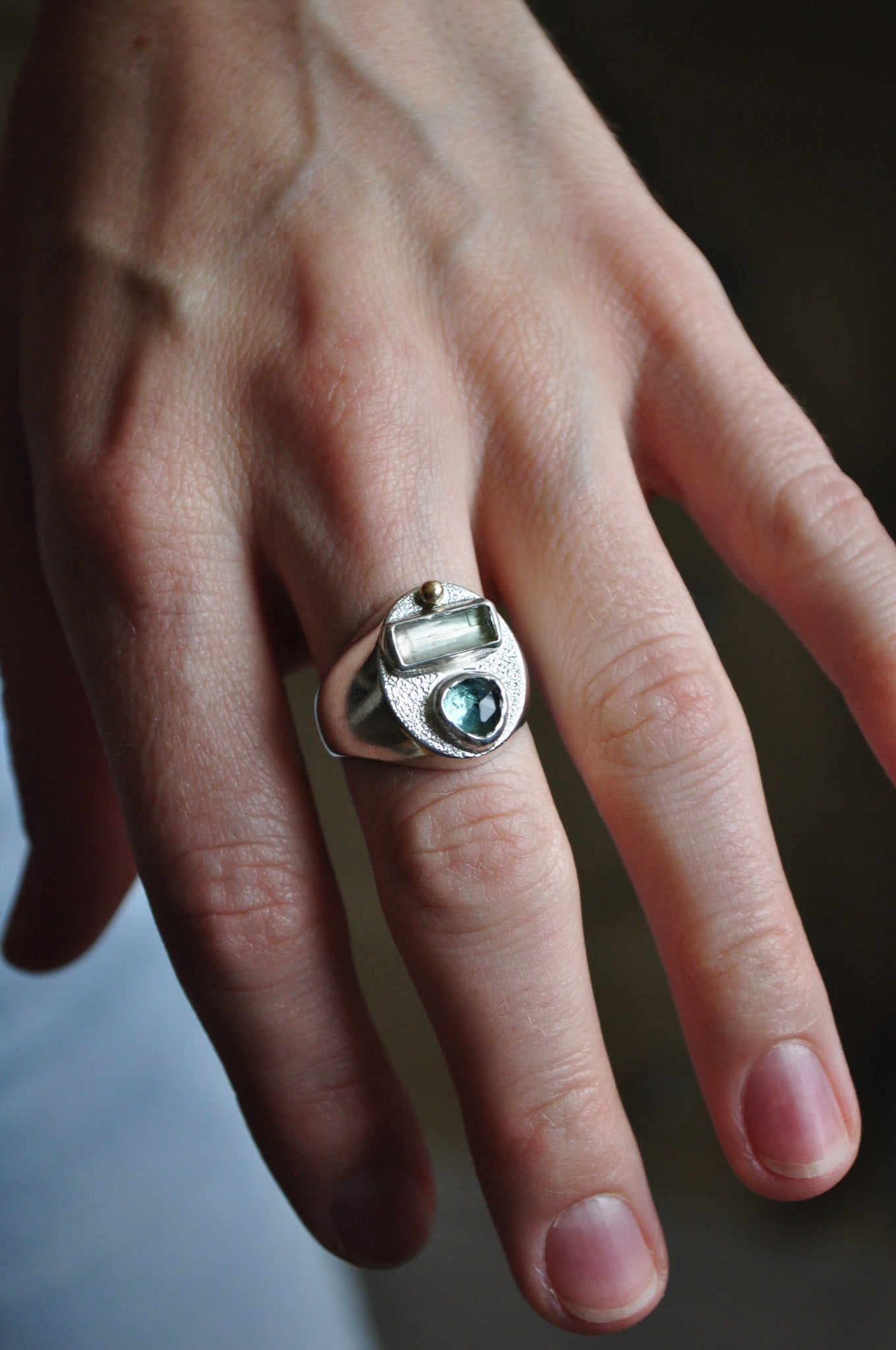 Close-up of a hand wearing a silver ring with a green gemstone on a blurred background