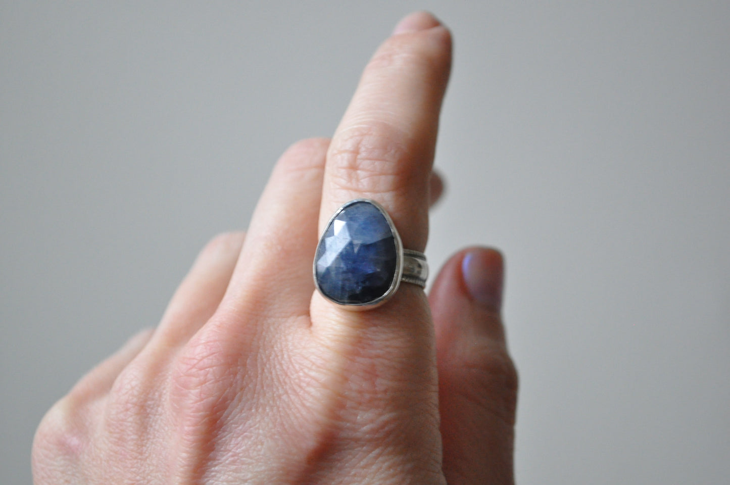 Hand wearing a ring with a blue stone on a neutral background