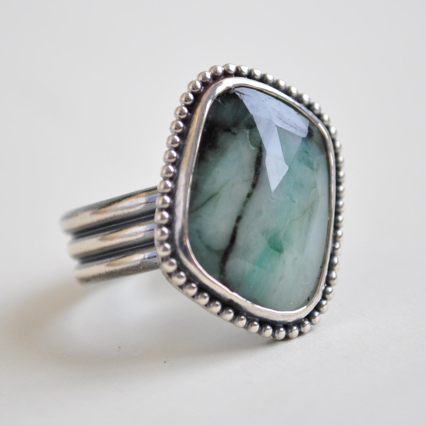 Silver ring with a large emerald stone on a light gray background
