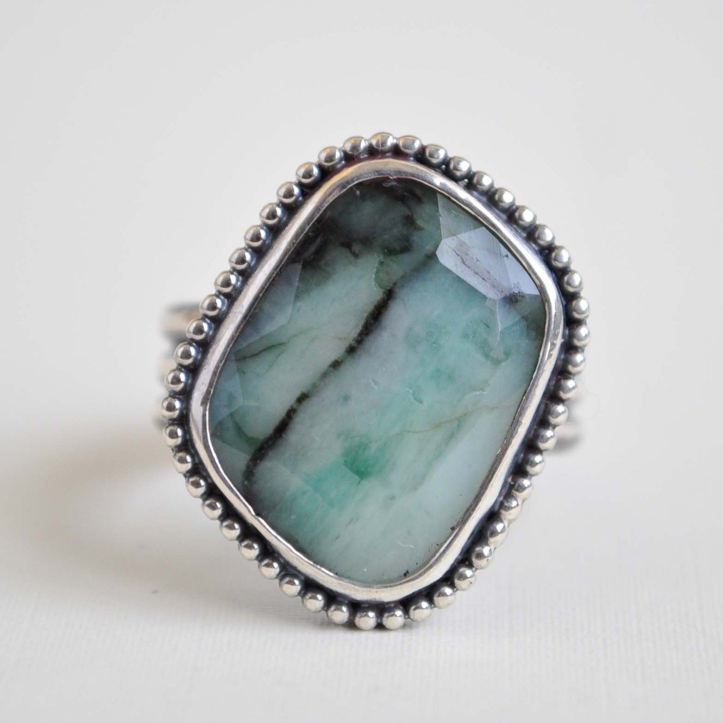 Ring with a large green stone and silver beaded band on a light background
