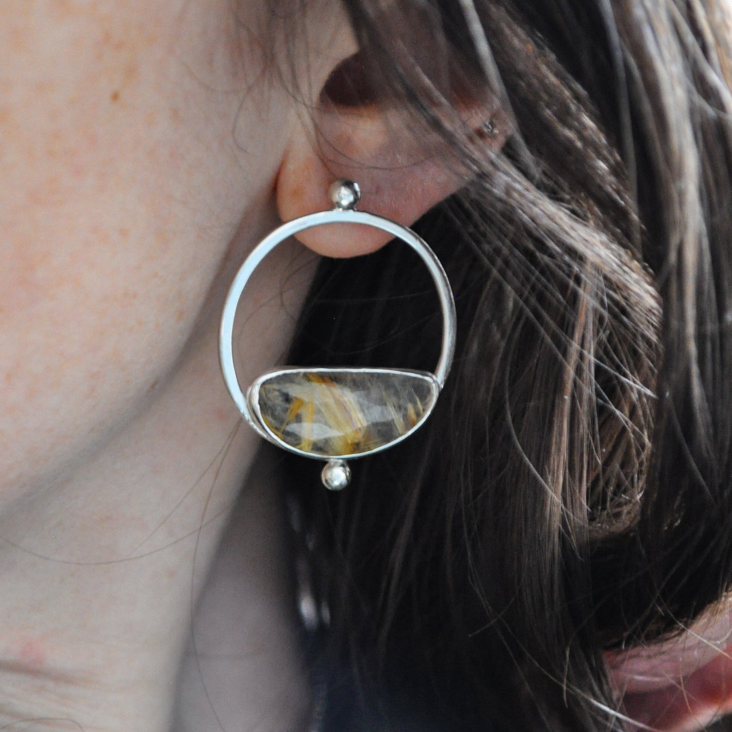 Close-up of a silver earring with a gemstone worn by a person.
