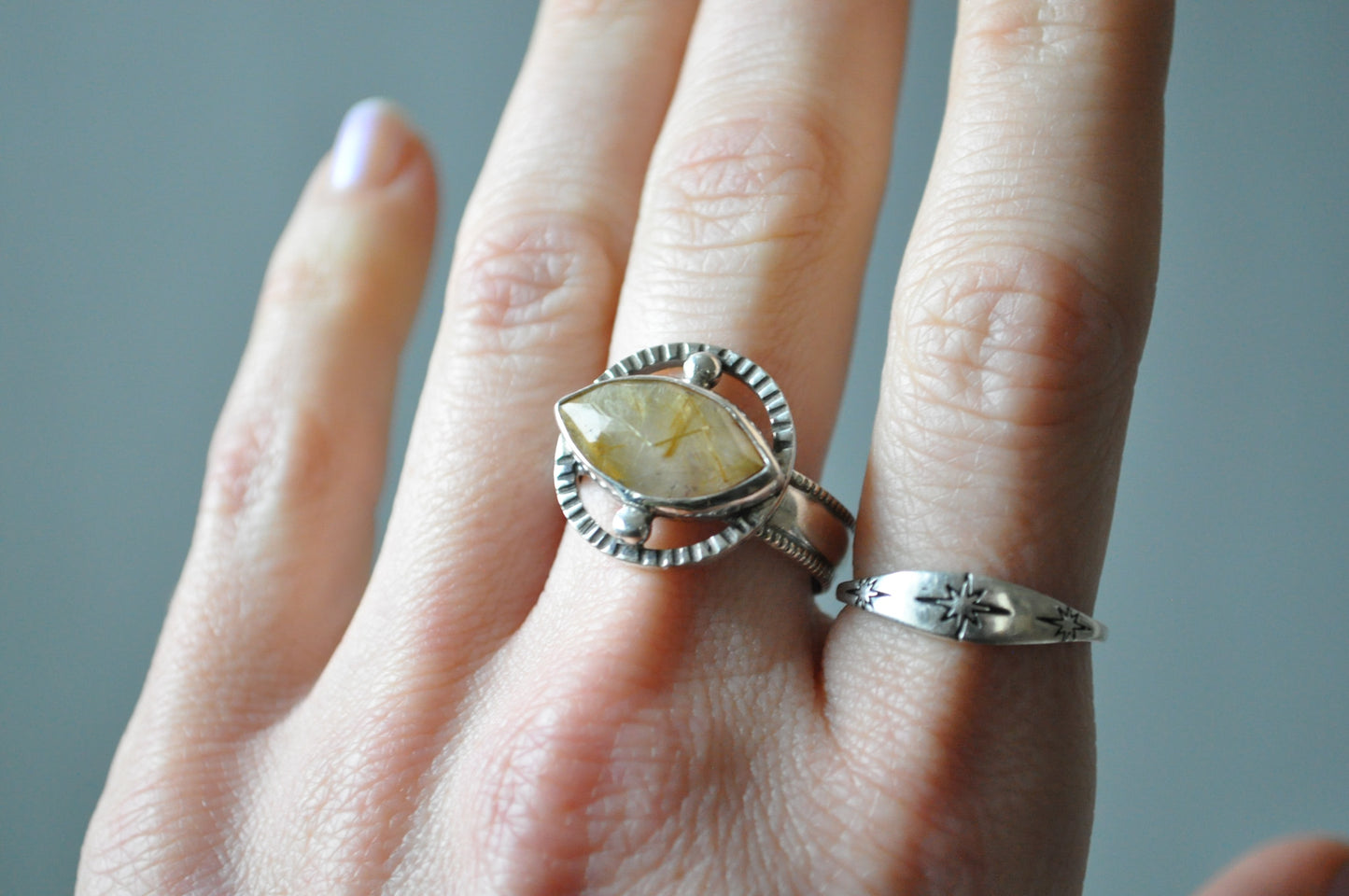 Hand wearing two silver rings with a yellow gemstone on a neutral background