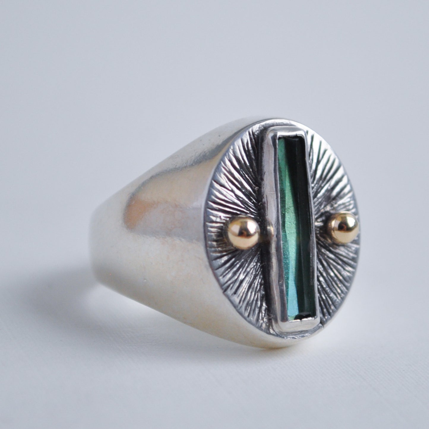 Silver ring with a green stone and gold accents on a light gray background