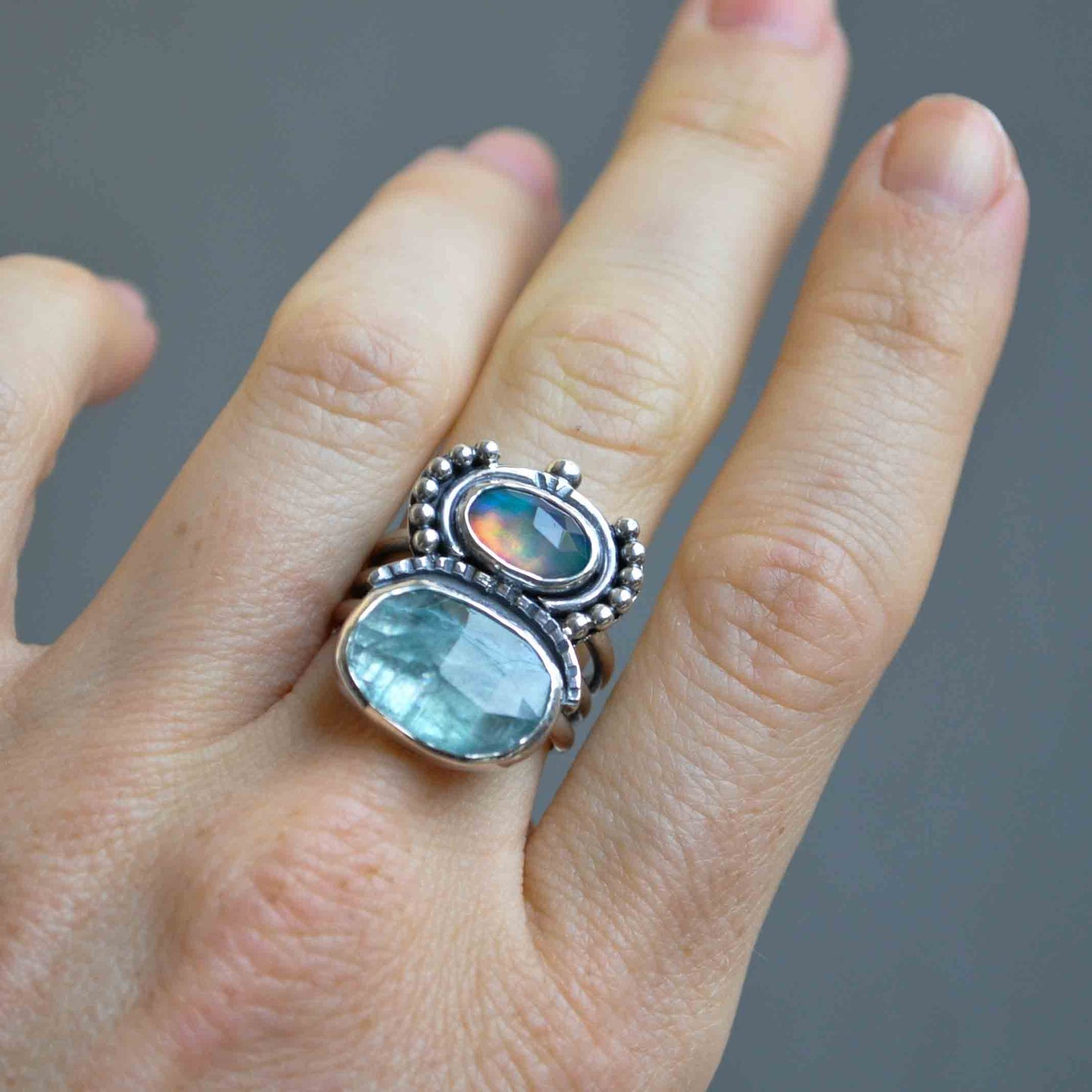 Ring with gemstones on a finger against a gray background