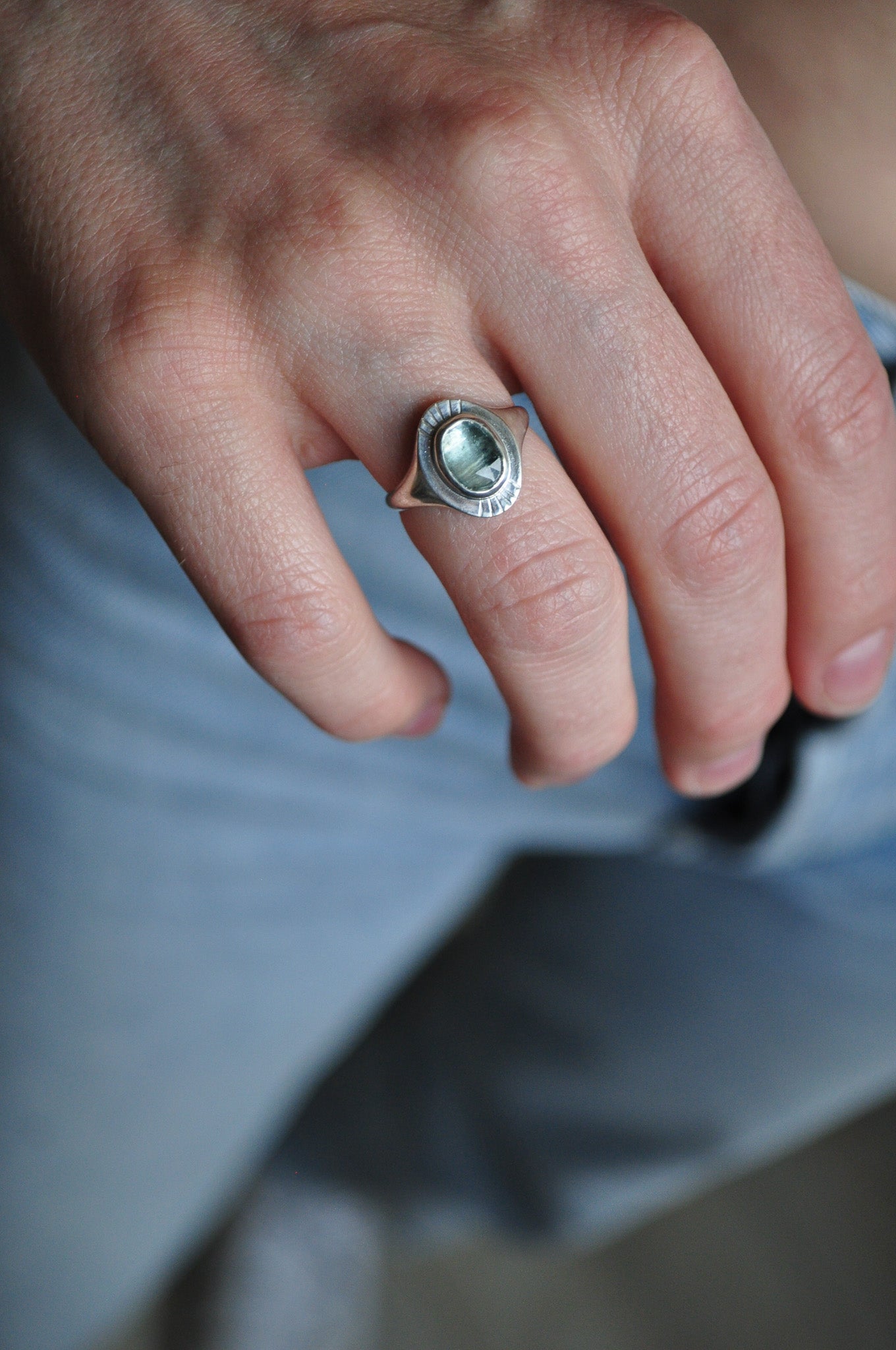 Close-up of a hand wearing a silver ring with a gemstone on a blurred background