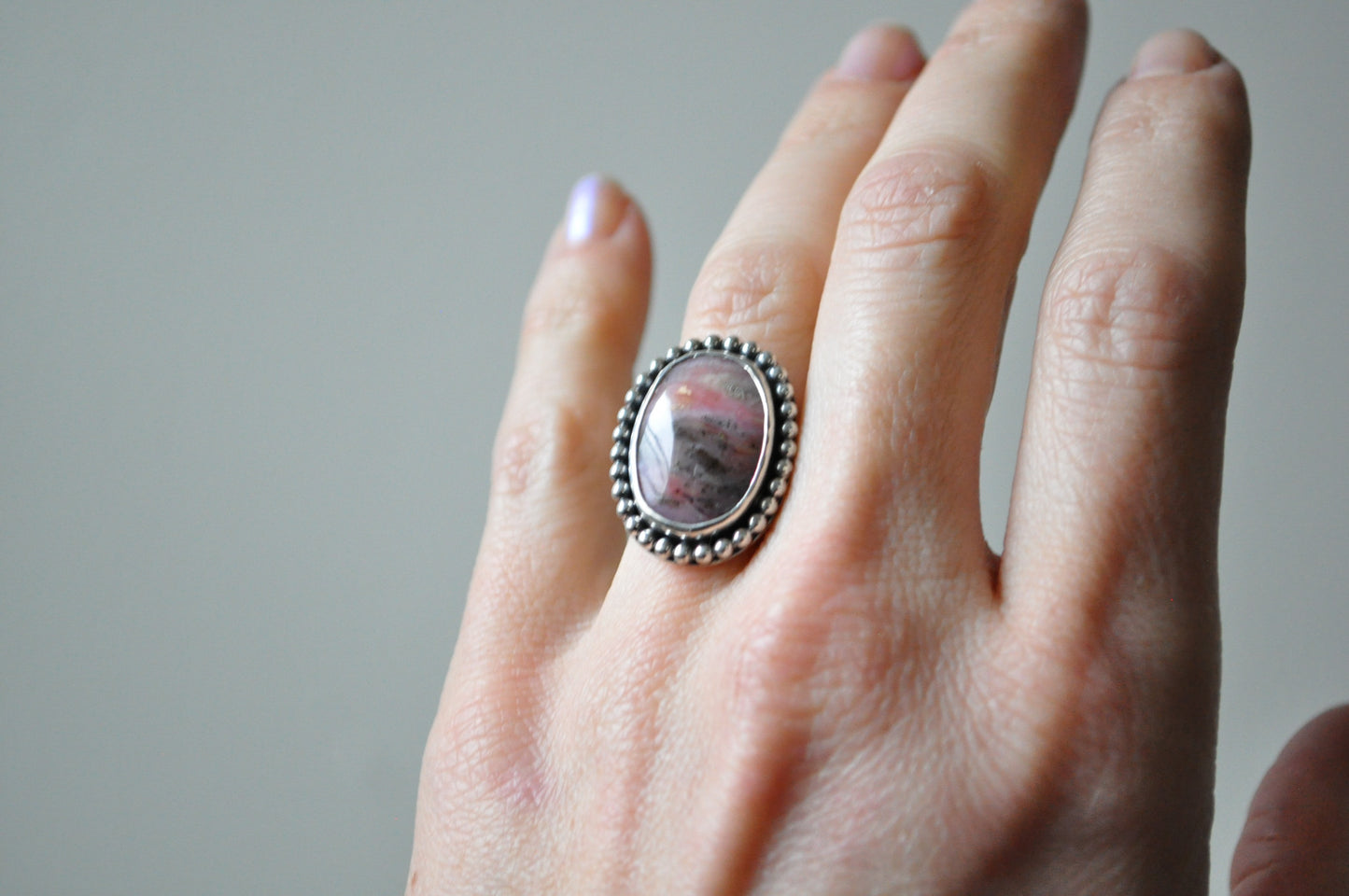 Hand wearing a ring with a stone on a neutral background