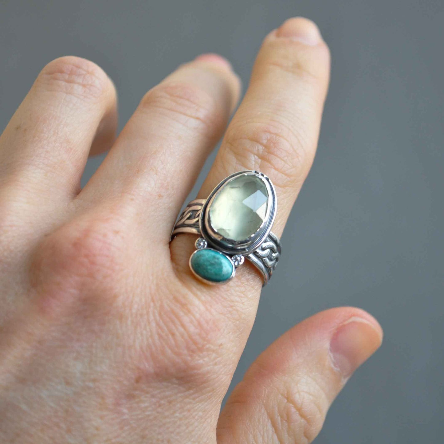 Hand wearing a silver ring with green gemstone on a gray background