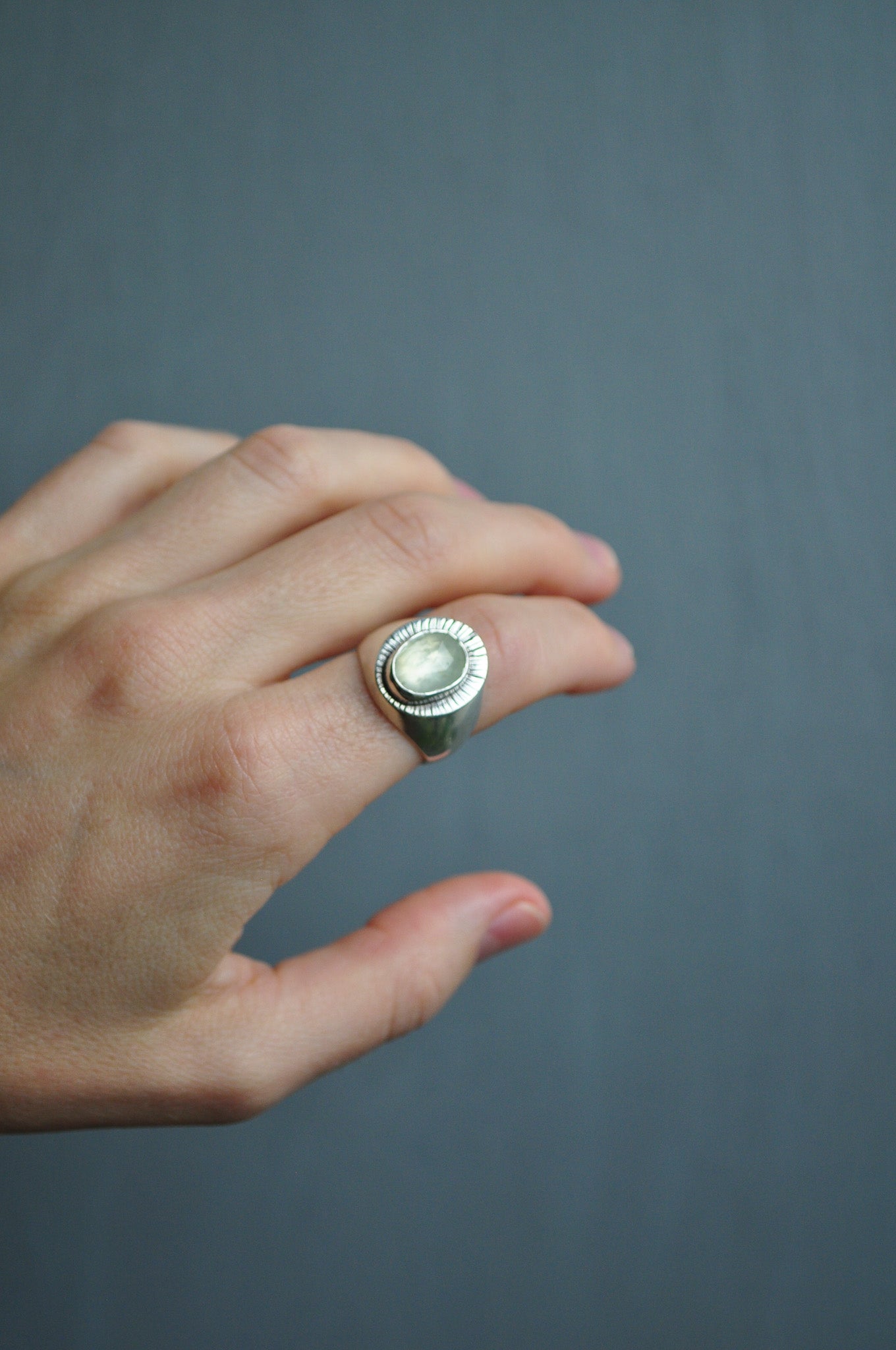 Hand wearing a silver ring with a dark gray background