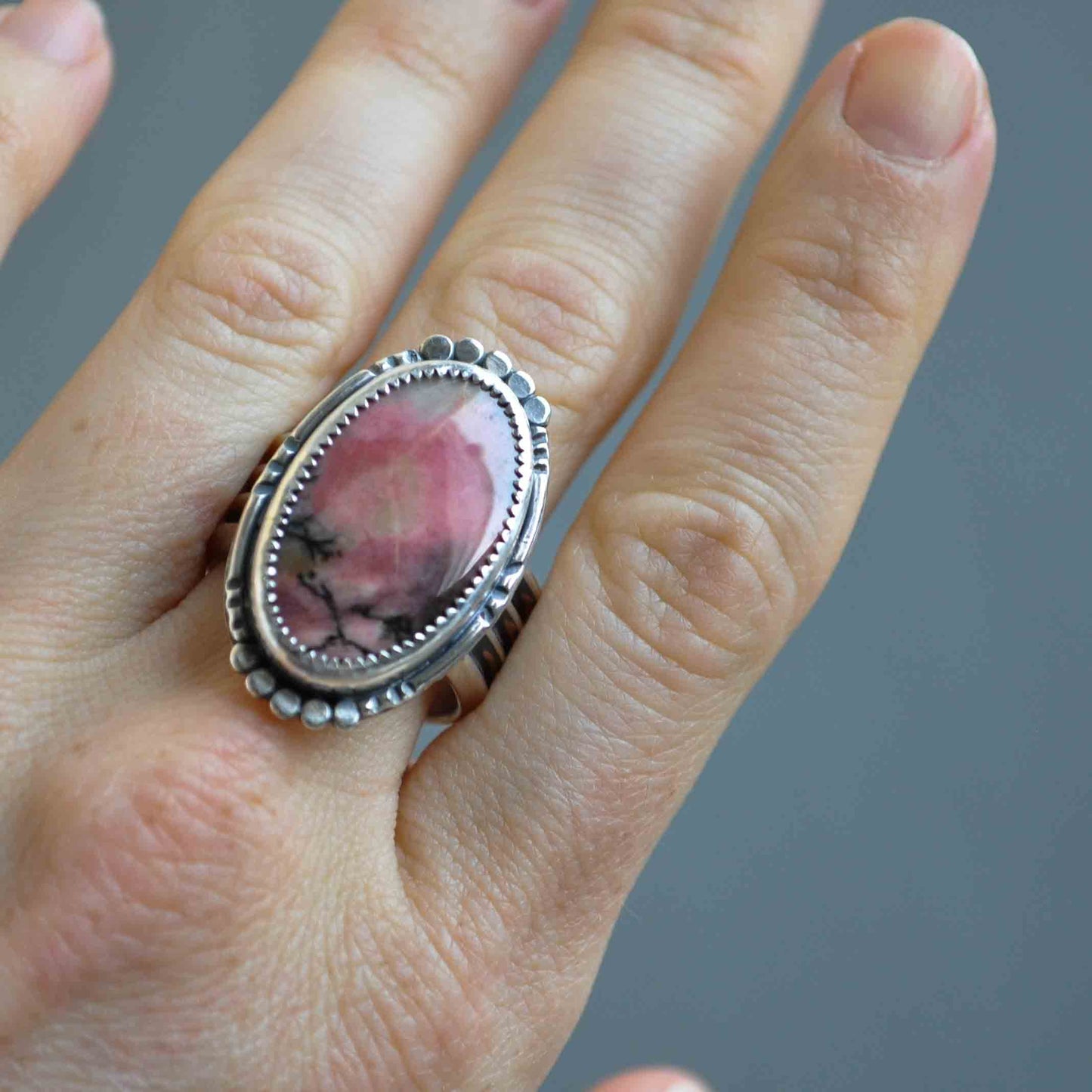 Silver ring with a pink stone on a hand against a gray background