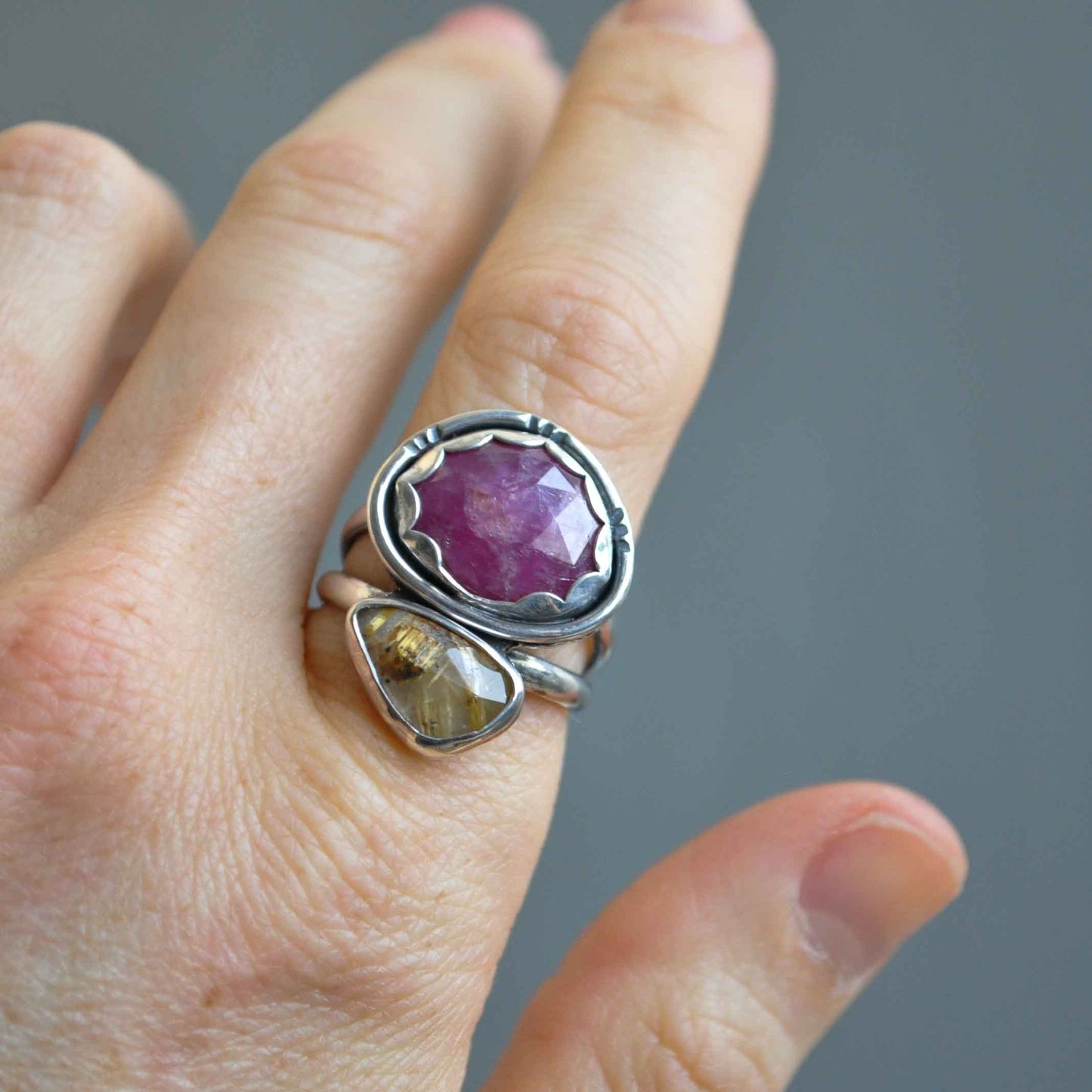 Silver ring with a purple gemstone on a finger against a gray background