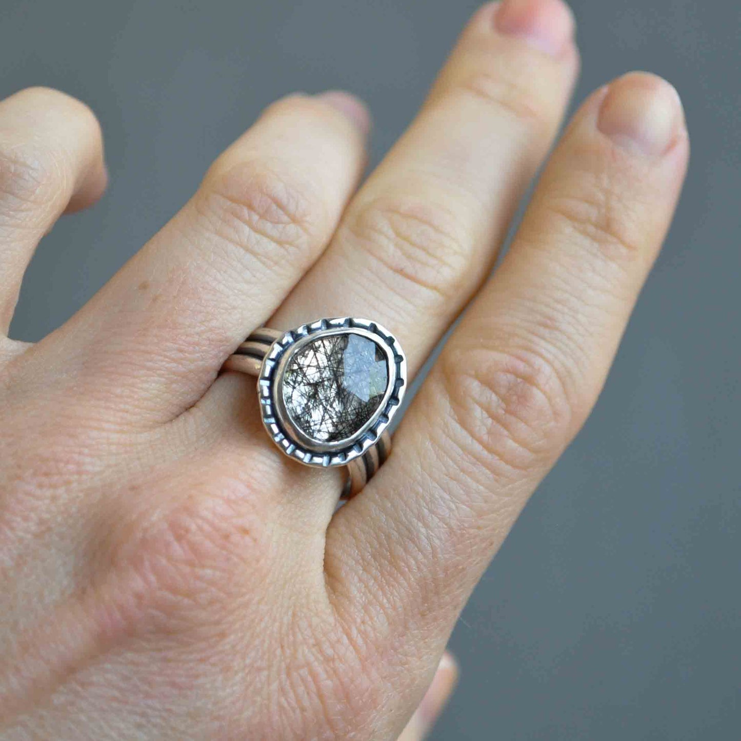 Hand wearing a silver ring with a stone on a gray background