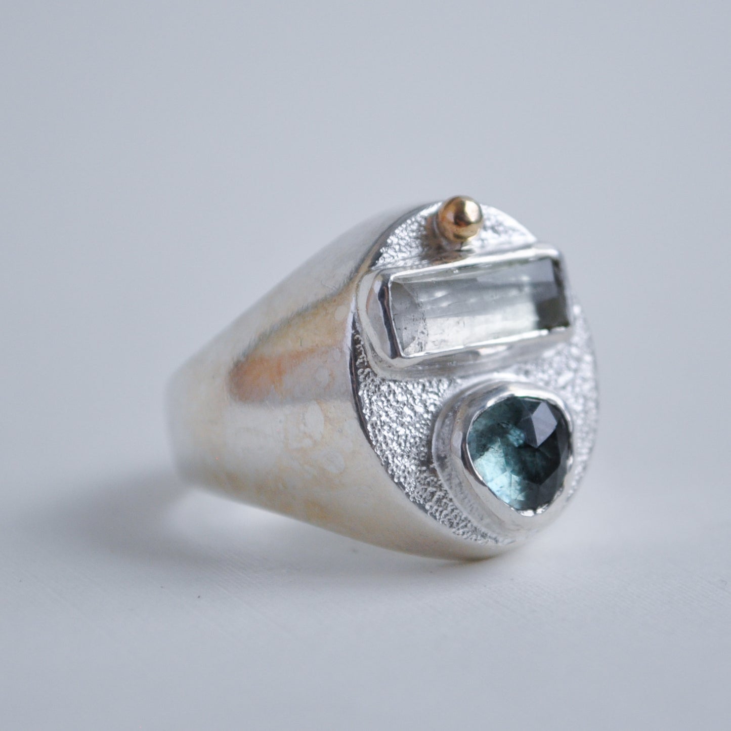 Silver ring with a blue gemstone and gold accents on a light gray background