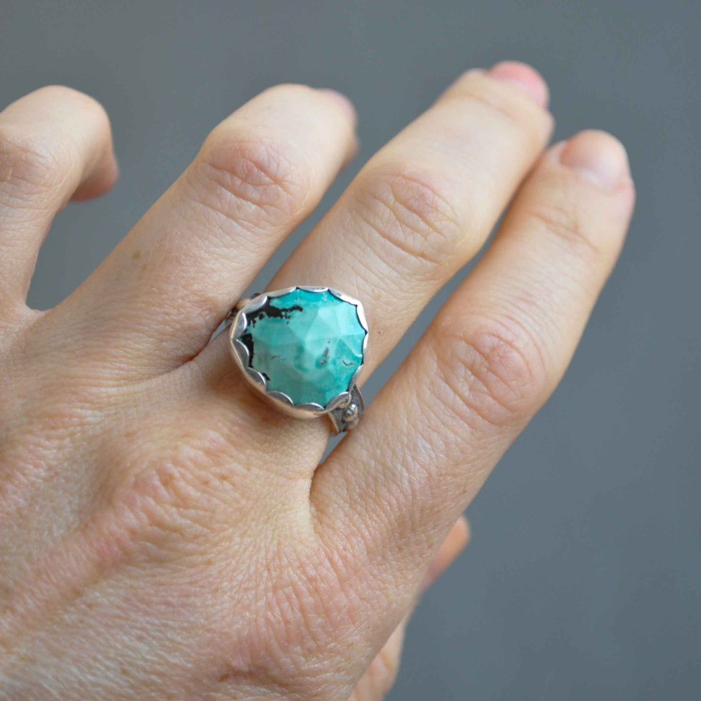 Turquoise ring on a finger against a gray background