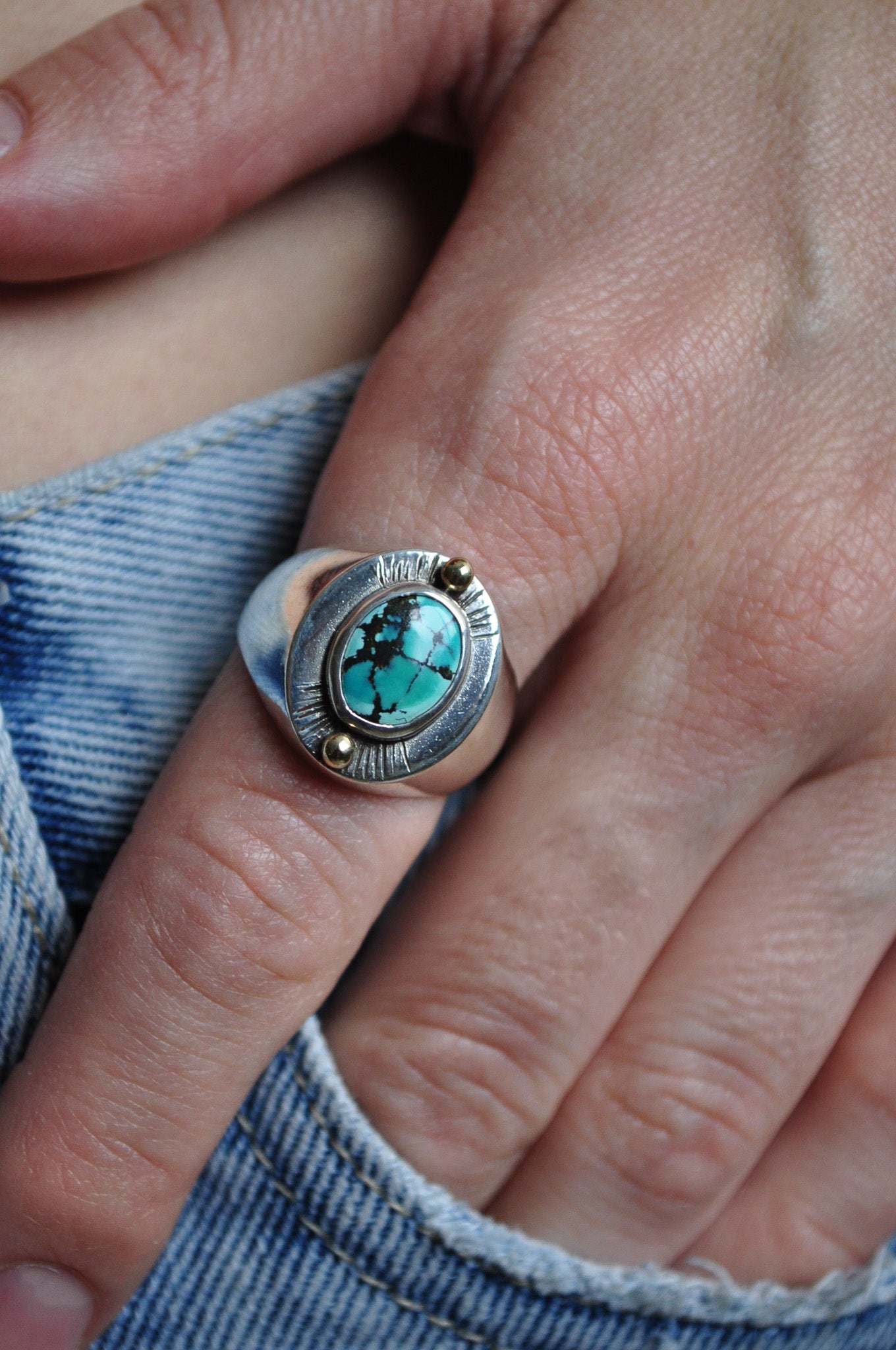 Close-up of a hand wearing a silver ring with a turquoise stone.