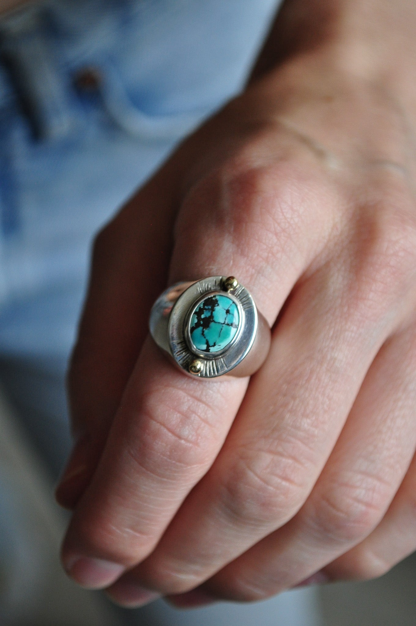 Close-up of a hand wearing a silver ring with a turquoise stone.