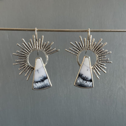 Pair of earrings with sunburst design and marble-like stone on a gray background