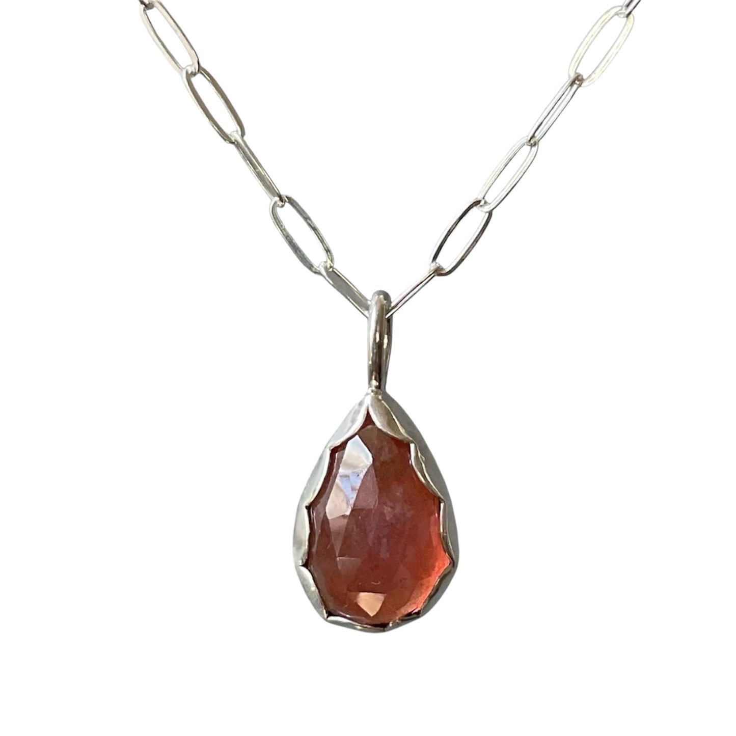 Teardrop-shaped pendant with a red stone on a silver chain against a white background