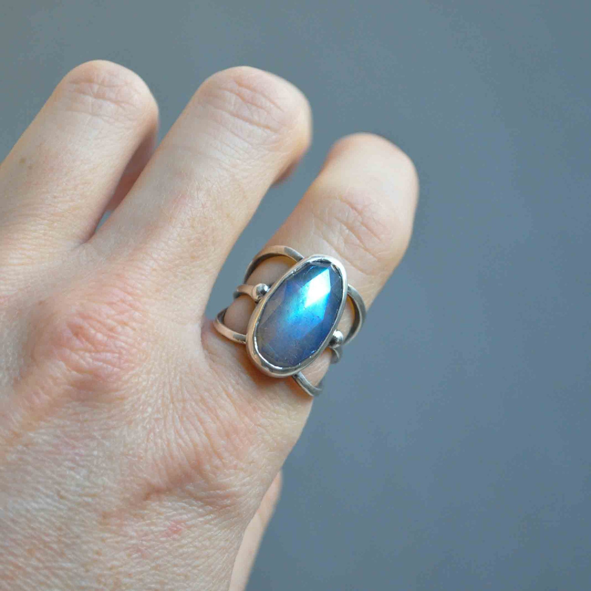 Hand wearing a silver ring with a blue gemstone against a gray background