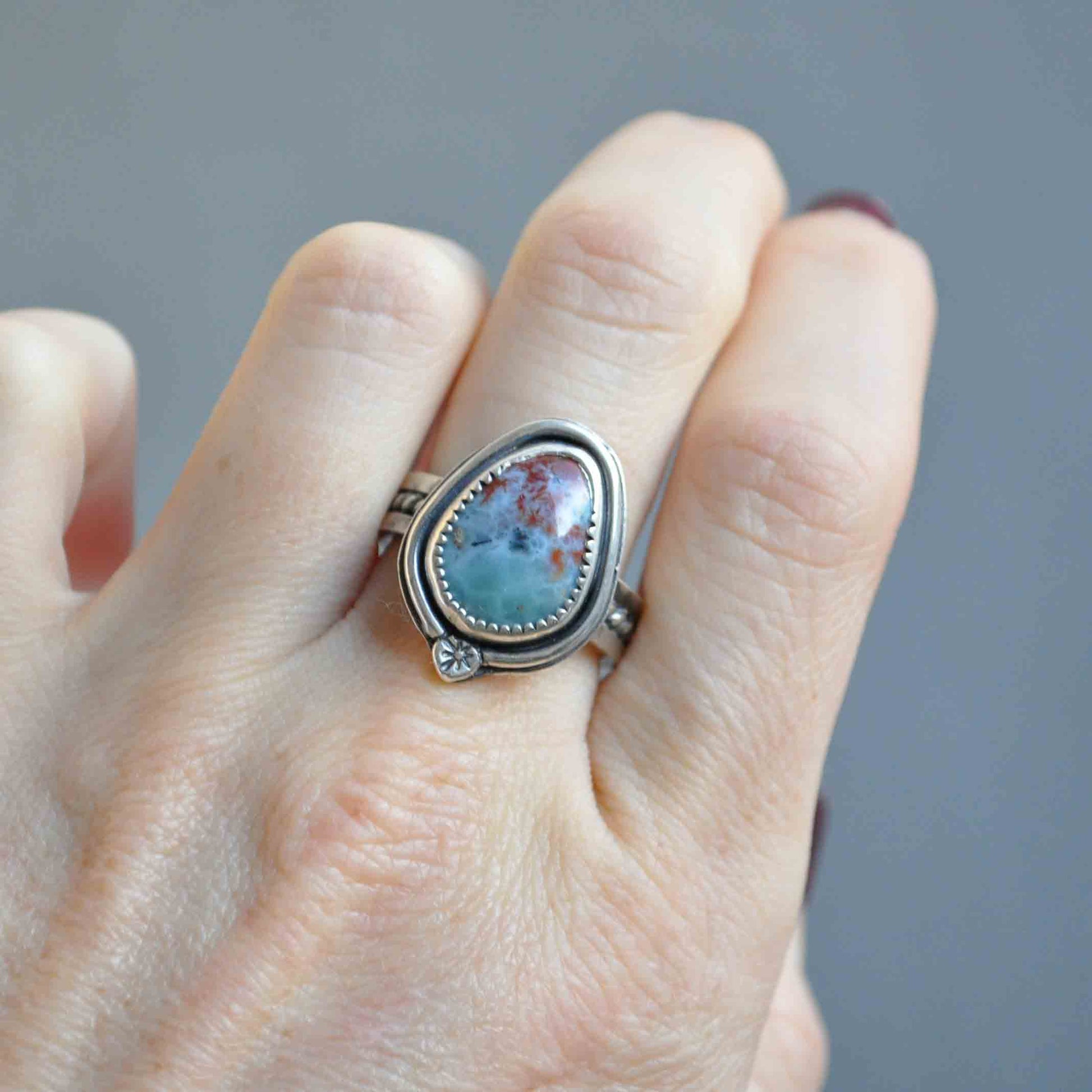 Silver ring with a turquoise stone on a finger against a gray background