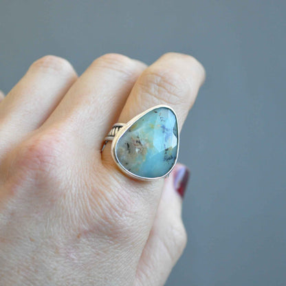 Hand wearing a ring with a large turquoise stone against a gray background