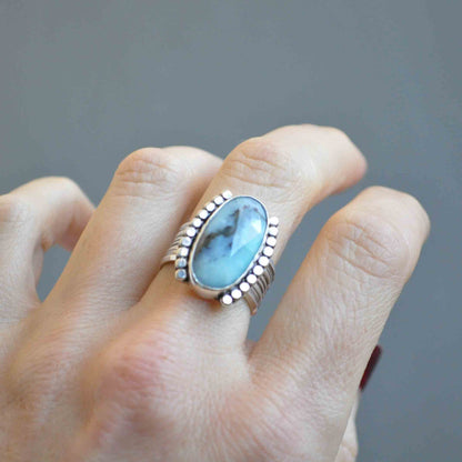 Ring with a blue stone on a finger against a gray background