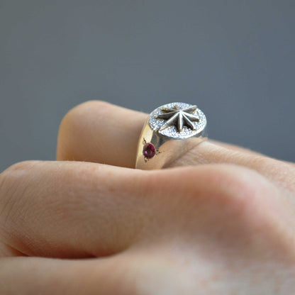 Close-up of a hand wearing a decorative ring with a red gemstone on a gray background