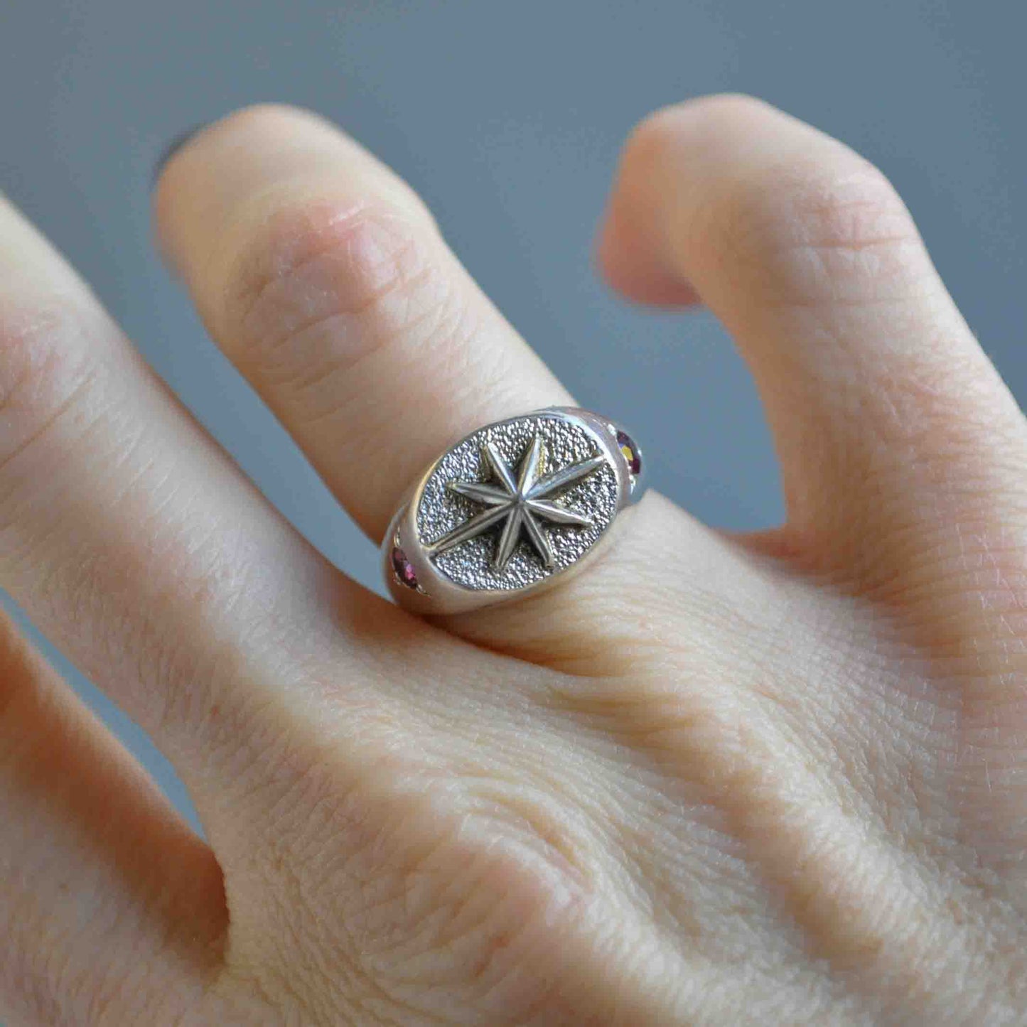 Silver ring with star design on a finger against a gray background
