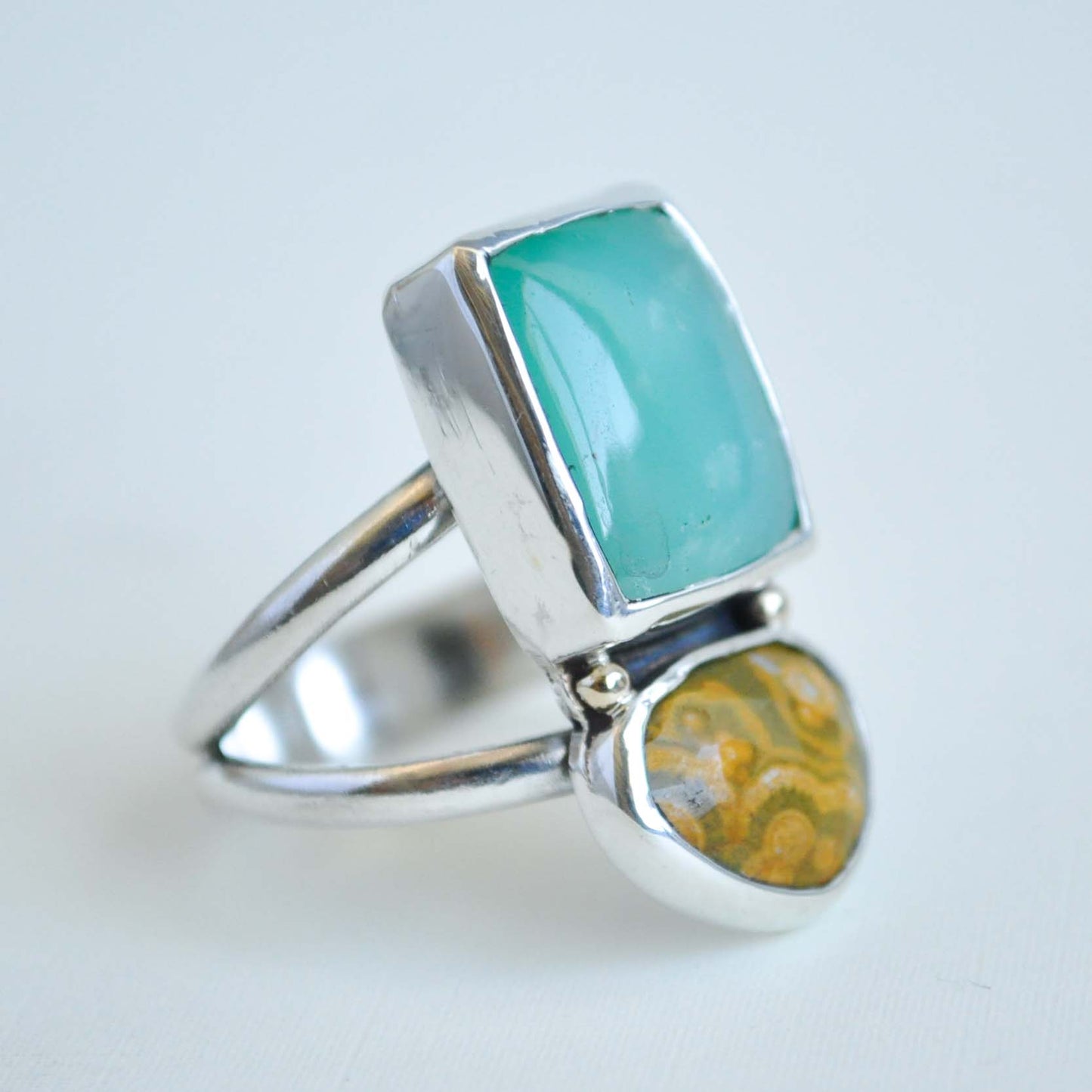 Silver ring with turquoise and yellow stone on a light gray background
