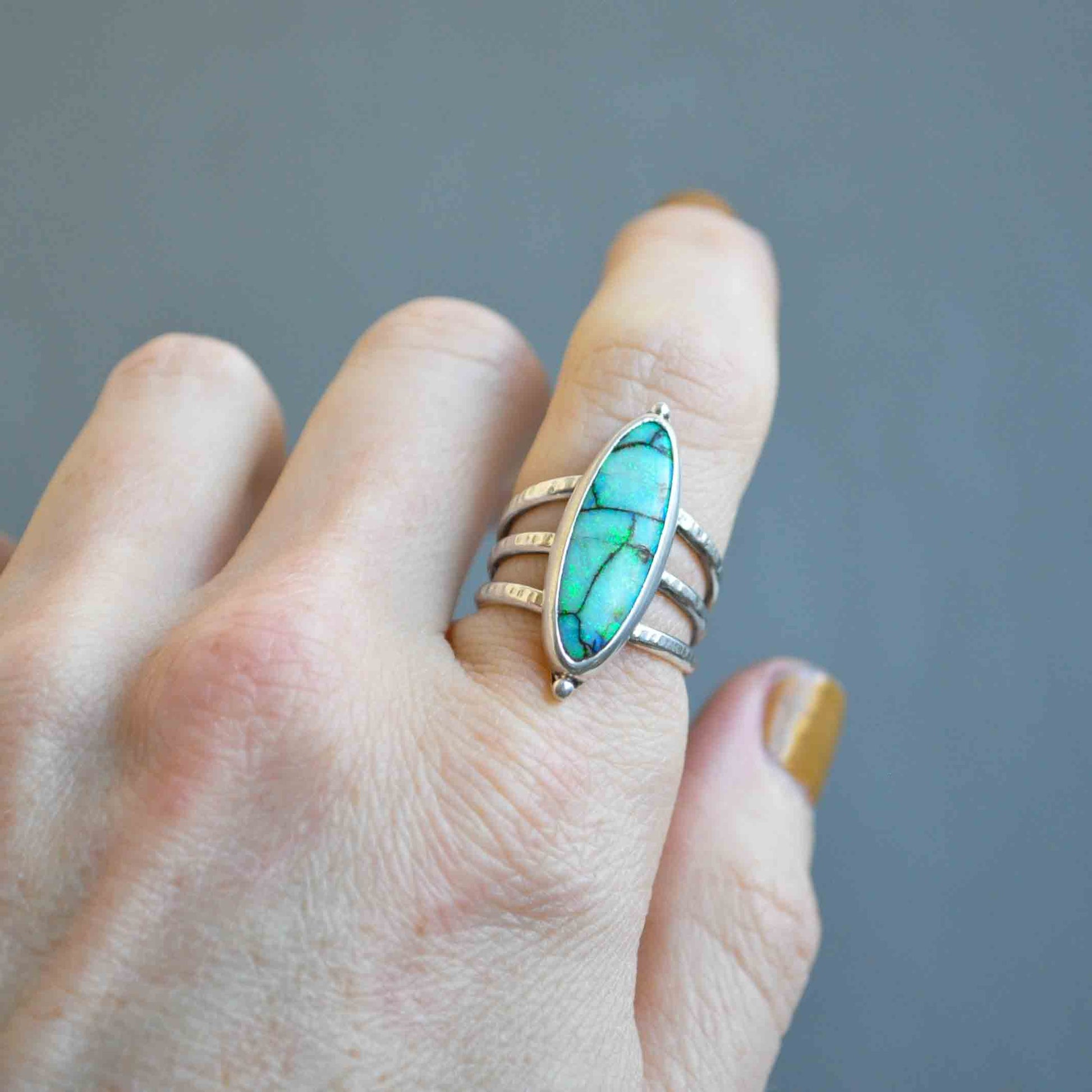 Turquoise ring on a finger against a gray background