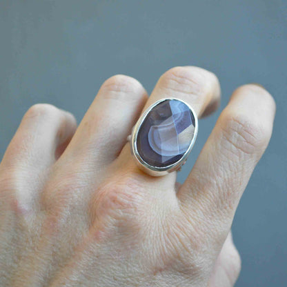 Hand wearing a ring with a purple stone on a gray background